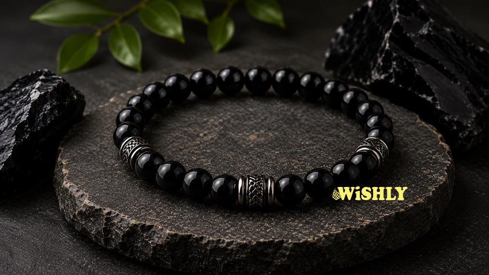 Obsidian bracelet with polished black volcanic glass beads displayed alongside natural obsidian stones on a dark textured surface.